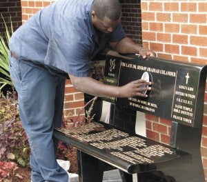 Don Garces places the finishing touch — a photo of the late Obadiah Colander — to a memorial bench honoring the founder of Faith Temple Ministries on Wellons Street. A memorial garden dedication will be held today at the church.