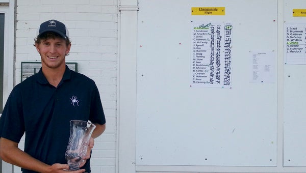 Suffolk’s John David Sanderson holds the winner’s cup while standing next to the final scoreboard for the 2013 Men’s Club Championship held by the Cedar Point Country Club for its members. Sanderson, 20, won the event for the fifth straight year, this time with a two-day score of 147.