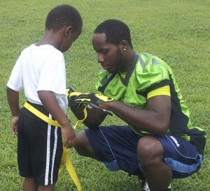 Suffolk Chargers defensive back Andre "AJ" Harper helps 5-year-old Damarrion Madison get prepared in a flag football game during the Peanut City Football Camp last weekend at the JFK Sports Complex. The kids took well to the Chargers players and want them to do more camps in the future. (Angela Harper photo)