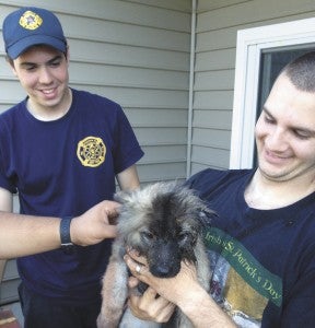 Carrollton volunteer firefighters Mason Halsey and Tyler Newton show off the pooch they freed from a drainage hole in a patio wall at the Eagle Harbor Apartments on Sunday.