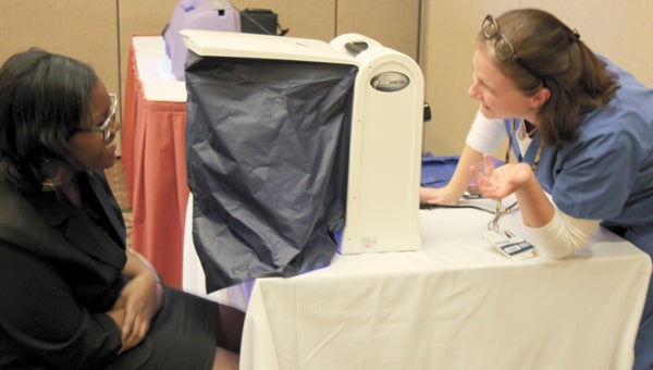 Sandy Buck, a cardiac rehabilitation nurse at Sentara Obici Hospital, tutors Nansemond River High School ninth-grader Charnise Knight on a machine that analyzes skin to detect skin cancer. Buck and Knight were among a large crowd of public school students and local business representatives at the downtown Hilton Garden Inn Thursday for the sixth annual Career and Technical Education Professional Student Conference.