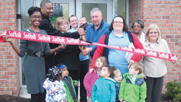 Mayor Linda T. Johnson, Councilman Roger Fawcett and business owner Willie Thompson work the scissors Wednesday to officially open Kids Kingdom Child Development Center in North Suffolk. They are joined by the center’s director, Amber Hines, as well as Jenna Robertson, with 3-month-old Elijah Burns, Tiffany Trojanowski, Loffie Goode and Marcia White. Peering up at the proceedings are Delores Lindsay, 2, Kevin Clarke, 2, Rebekah Wise, 3, Jaeliyah Jones, 2, Westyn Burgess, 1-1/2, and Joseph Wise, 3.