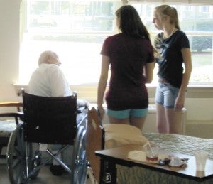 Jessica Bruner and Grace Fowler, who attended Alyssa Rose’s party, hand a flower to a local nursing home resident.