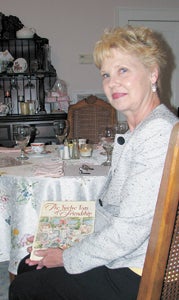 Diane Kippes shows off the book that inspired her to open a tea room as she sits at a downstairs table at Stillwater House.