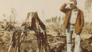 A man shows off the aftermath of a 1975 fire in the refuge, with a dotted line marking the peat level before the fire. (Courtesy Great Dismal Swamp National Wildlife Refuge)