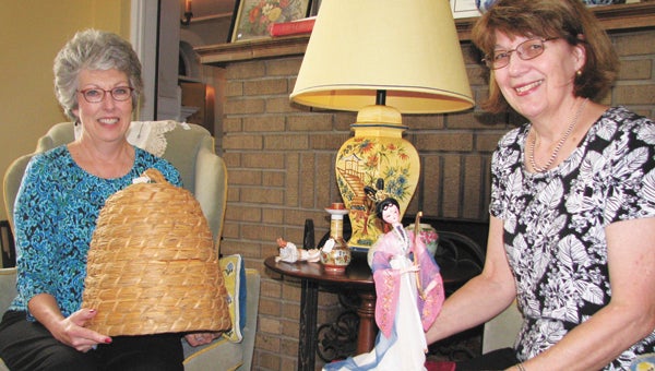Suffolk Nansemond Historical Society member and volunteer Julie Johnson, left, and vice president Lynn Cross show off some of the items that are up for grabs in the society’s heirloom sale next weekend, including the bee skep Johnson is holding, the doll Cross is holding, the lamp between them and the wingback chairs in which they’re sitting.