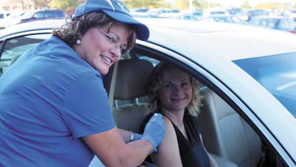 With her “patient,” fellow registered nurse Angela Couci, registered nurse Ellen Cutchins shows how free flu shots will be given through the car window during a drive-through-free-flu-shot session at Bon Secours Health Center at Harbour View on Sept. 27.