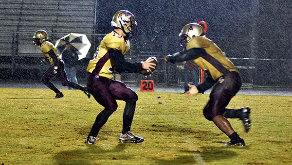King’s Fork High School senior quarterback Ryan Kluck hands the ball off to senior feature back Deshaun Wethington as the rain falls on Friday night. Wethington’s 168 yards and a strong defensive performance gave the Bulldogs a 14-6 home win over Western Branch High School. (Caroline LaMagna photo )